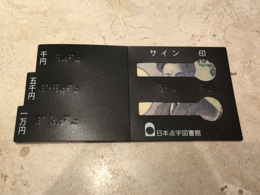 千円札をこの紙幣見分け板に重ね合わせると、千円札の横方向の長さが見分け板の「千円」のところにぴったり一致するのが分かる写真イメージ