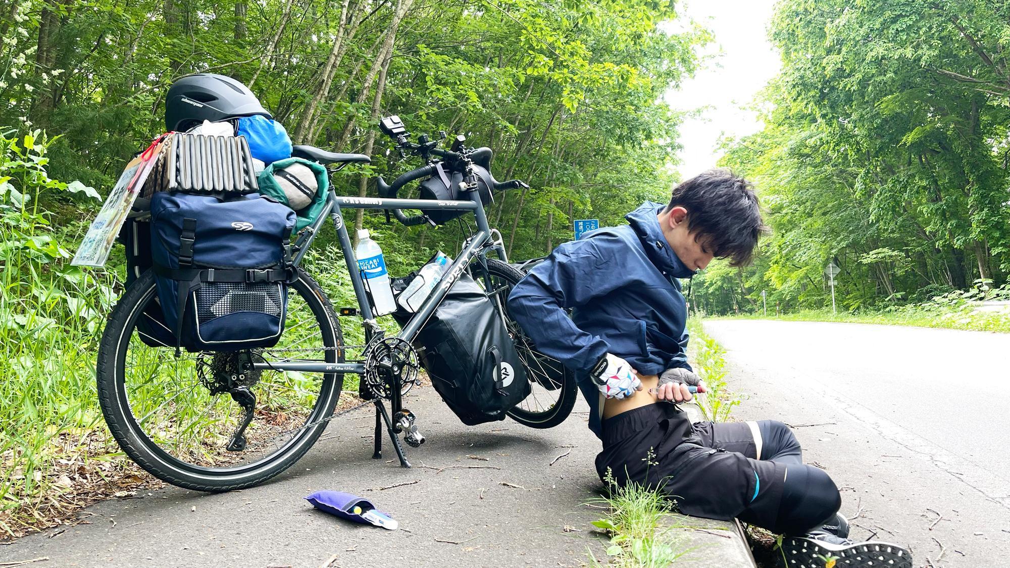 林が続く道路の脇で注射をする本間さん