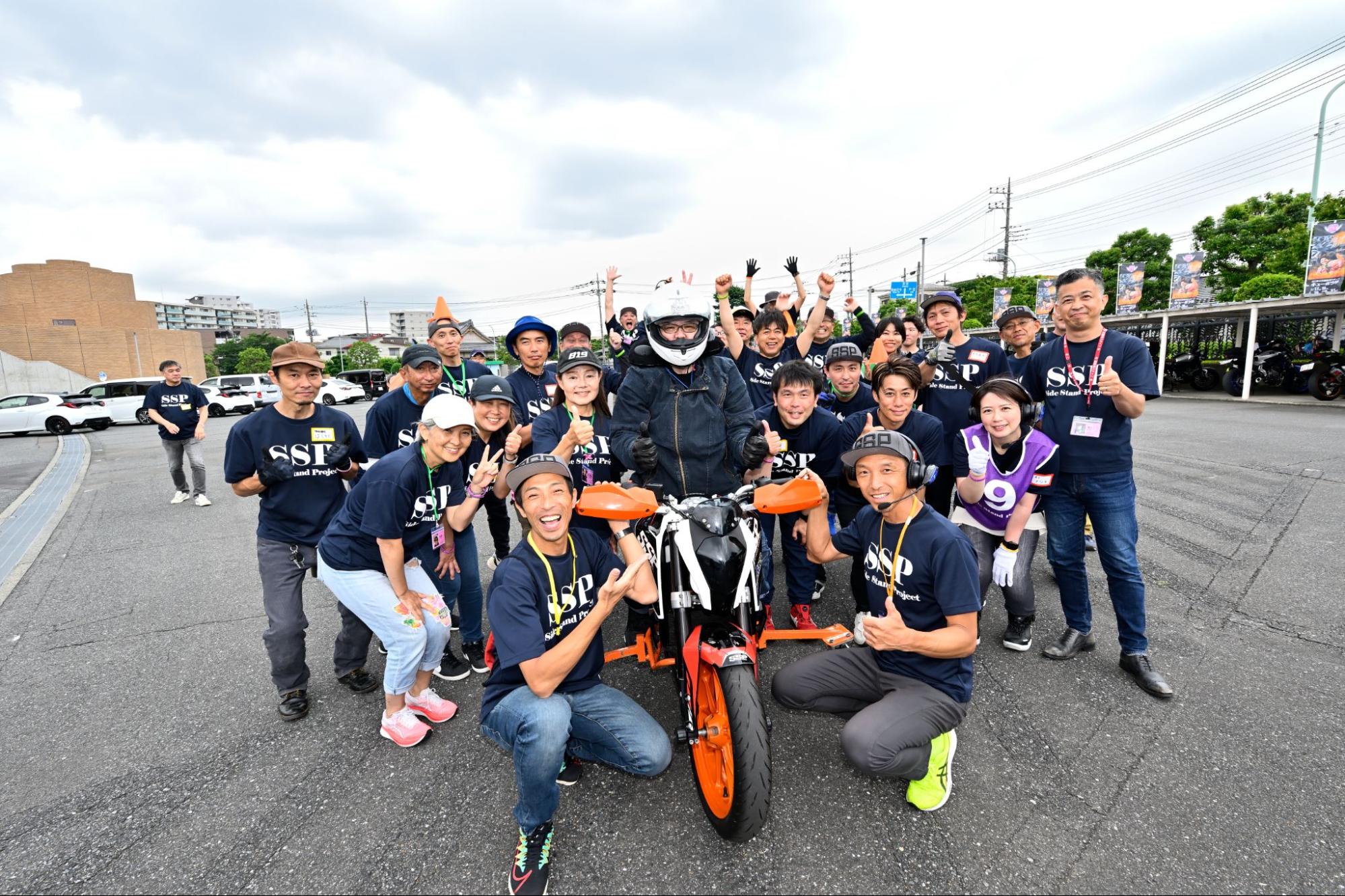バイクとライダーを囲んで、20名ほどの笑顔の集合写真